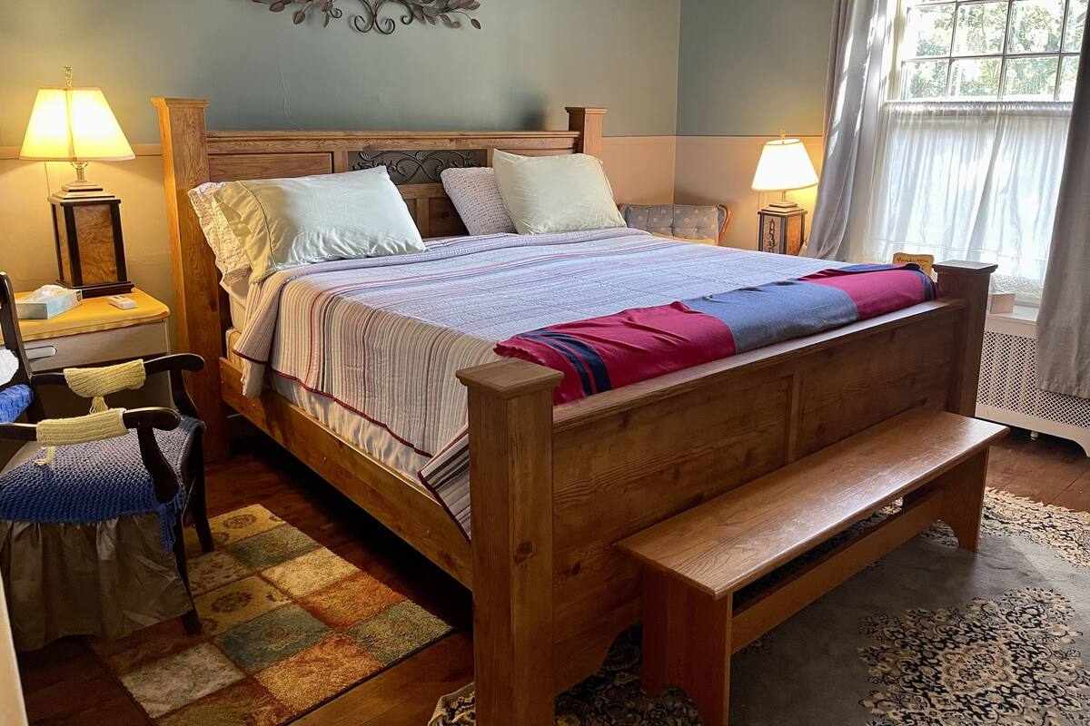 Un lit en bois avec une banquette, deux tables de chevet, une chaise et un élément décoratif mural.