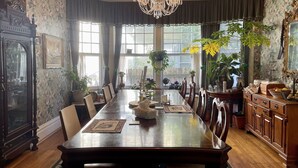 A dining room with a long wooden table, chairs, a chandelier, and various plants. - Greenwood Bed & Breakfast (Greensboro)