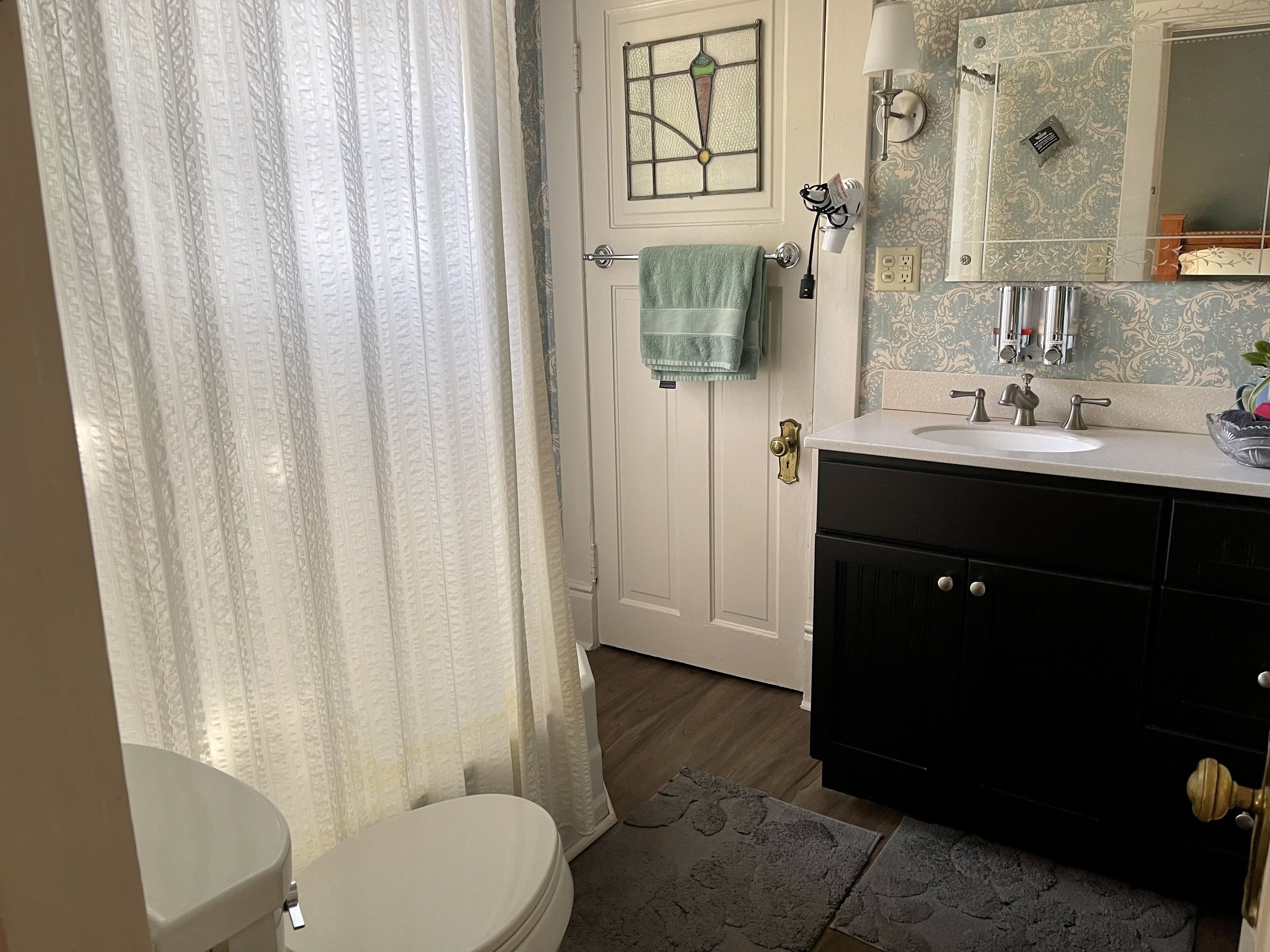 Een badkamer met een wit toilet, een wastafel met spiegel en een handdoek aan de deur.