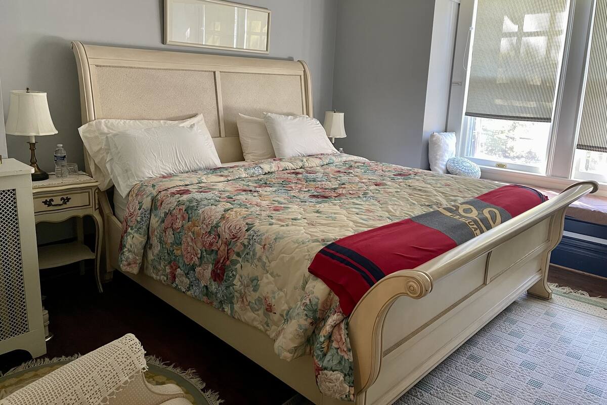Une chambre à coucher bien rangée, avec un lit, des tables de chevet, des lampes et une fenêtre équipée de stores.
