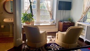 A room with a large window, a television, a potted plant, and two chairs. - Greenwood Bed & Breakfast (Greensboro)