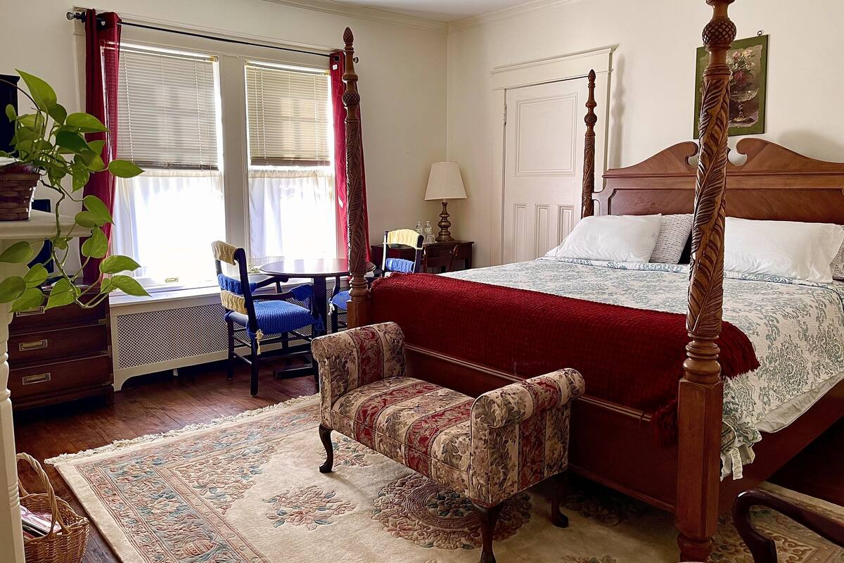 Une chambre à coucher avec un lit à baldaquin, une chaise, un bureau et une fenêtre avec des rideaux.