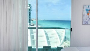 A room with a large sliding glass door leading to a balcony with a view of the ocean and a cityscape. - Ocean view studio, great views, balcony, beach, pool, gym, jacuzzi (Cancún)