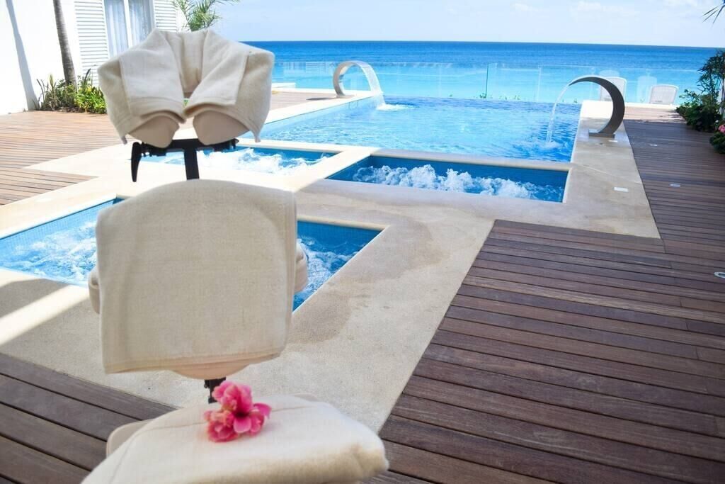 A pool area with a view of the ocean, a wooden deck, and lounge chairs.