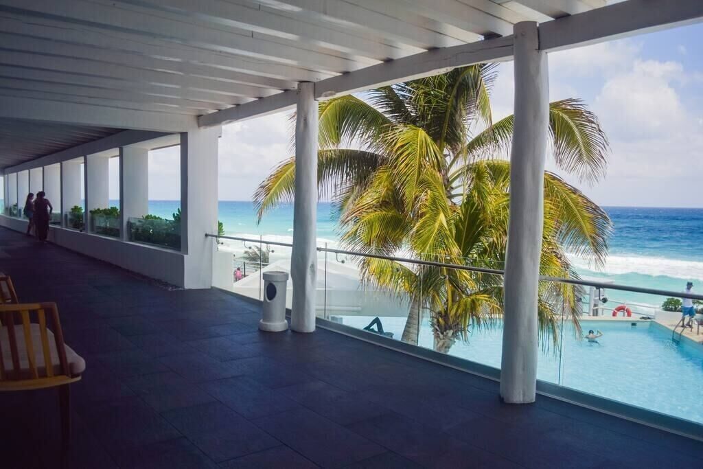 A covered outdoor area with a pool, palm trees, and a view of the ocean.