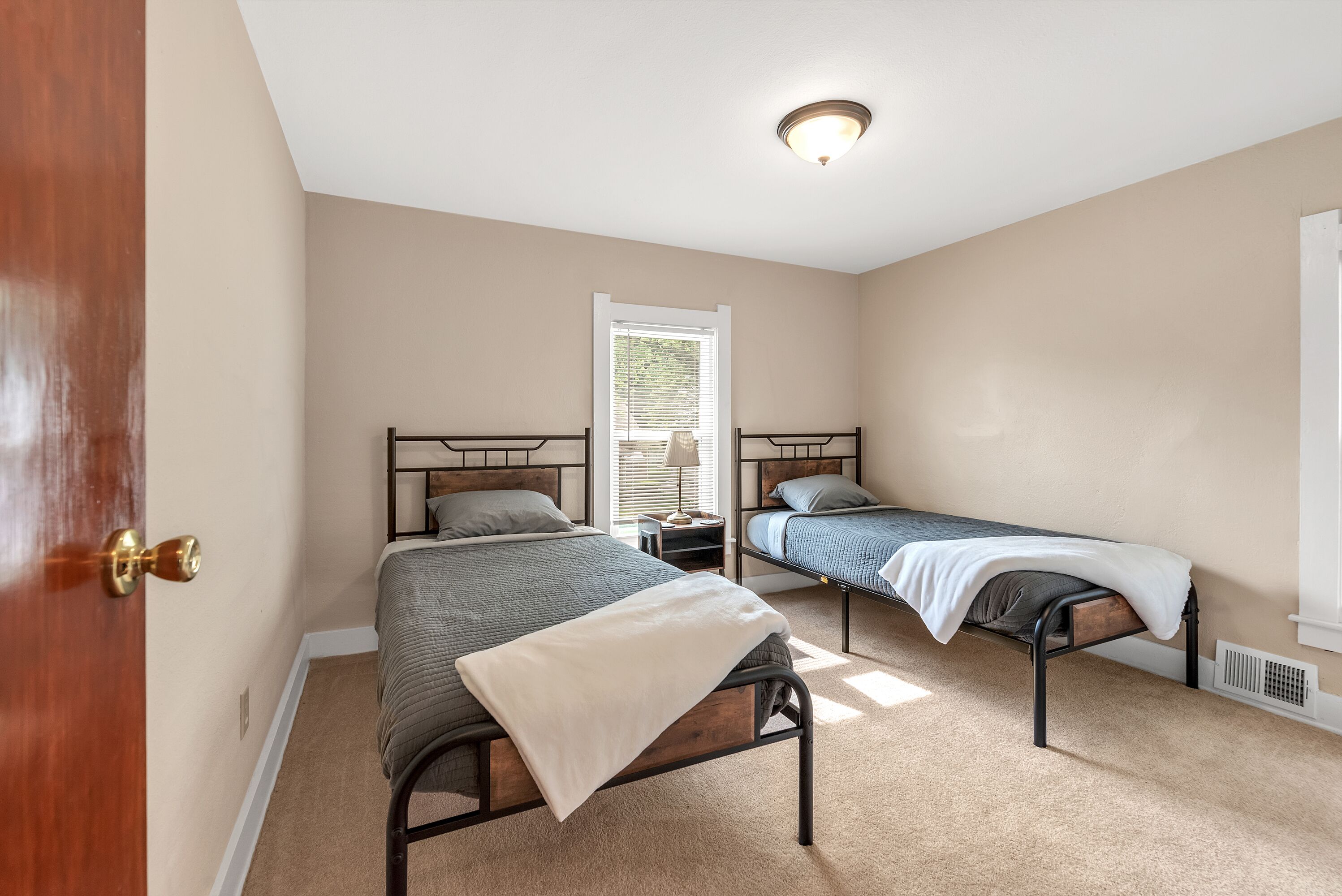 A bedroom with two beds, a door, a window with blinds, and a ceiling light fixture.