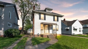 Ein zweistöckiges Haus mit Veranda, Backsteinkamin und gepflegtem Rasen.
