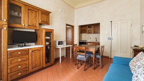 A compact kitchen with wooden cabinets, a microwave, and a dining area with a table and chairs. - Inferno Double - One Bedroom Apartment, Sleeps 2 (Firenze)