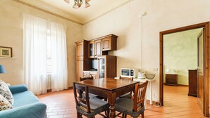 A dining area with a wooden table and chairs, a kitchen with cabinets and appliances, and a blue sofa with patterned cushions. - Inferno Double - One Bedroom Apartment, Sleeps 2 (Firenze)