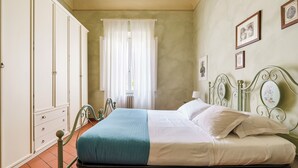 A bedroom with a bed, a wardrobe, a window with curtains, and wall-mounted pictures. - Inferno Double - One Bedroom Apartment, Sleeps 2 (Firenze)