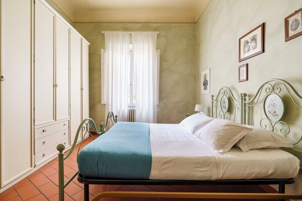 Un dormitorio con cama, armario, ventana con cortinas e imágenes colgadas en la pared.
