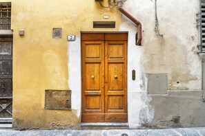 Una puerta doble de madera con una placa con el número '7' encima, ubicada en un edificio de fachada amarilla y blanca.