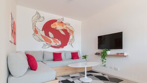 Un salon moderne avec un canapé, une table basse ronde, un téléviseur fixé au mur et une grande fresque représentant des poissons koï.