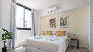Une chambre d’hôtel avec un lit, une table de chevet, une plante en pot et deux œuvres d’art encadrées accrochées au mur.