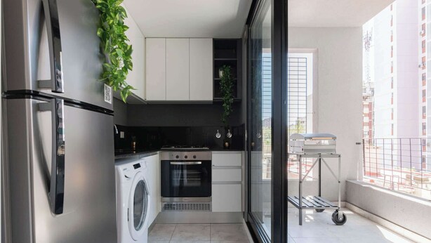 Une cuisine compacte équipée d’un lave-linge, d’un four et d’un petit coin repas avec vue sur l’extérieur par une fenêtre.