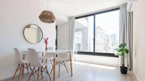 Un espace repas moderne avec une table blanche, quatre chaises, un miroir rond et un luminaire suspendu.