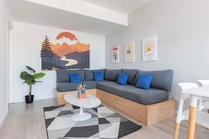 A modern living room with a grey sectional sofa, blue cushions, a white coffee table, and a large abstract painting on the wall.