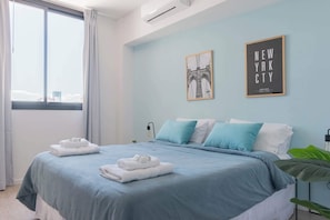 Quarto de hotel moderno com uma cama grande, vista da cidade e uma fotografia emoldurada de uma ponte.