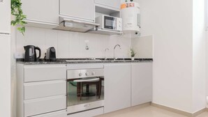 Una cocina moderna con armarios blancos, microondas integrado, hervidor y cafetera.