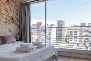 Ein Hotelzimmer mit Bett, Fenster mit Blick auf die Stadt und Wand mit Blättermuster.