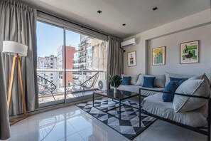 Ein modernes Wohnzimmer mit einer Couch, einem Couchtisch und Blick auf die Stadt durch große Fenster.