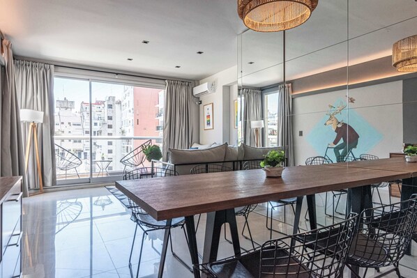 Ein moderner Essbereich mit einem Holztisch, schwarzen Stuhlgestellen aus Draht und Blick auf die Stadt durch große Fenster.