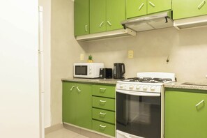 A kitchen with green cabinets, a white microwave, a black coffee maker, and a white stove.