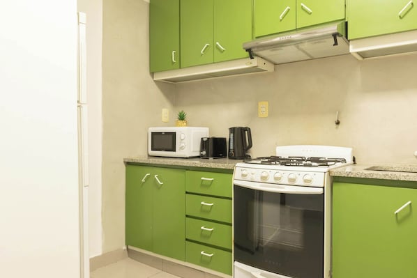 A kitchen with green cabinets, a white microwave, a black coffee maker, and a white stove. - MOT Rentals + Juncal 2800 - 2 Bd in Alto Palermo (Recoleta)