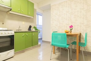 A kitchen with green cabinets, a white stove, and a dining area with a wooden table and turquoise chairs.