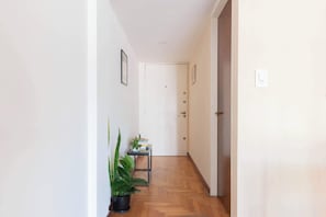 A hallway with a wooden floor, a small table with books and a plant, and a door at the end.