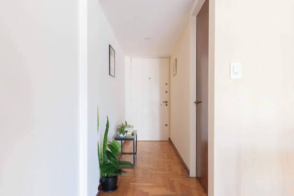 A hallway with a wooden floor, a small table with books and a plant, and a door at the end.