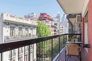 Ein Balkon mit Korbstühlen und einem kleinen Tisch mit Blick auf eine Stadtlandschaft und verschiedenen Gebäuden.