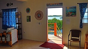 A room with a view of the sea, a door leading outside, a chair, a shelf with items, and a red mat. - Waterfront 2 Bedroom/ 2 bath POOL home w/ Stunning Ocean Views!! (Caye Caulker Village)