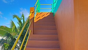 A staircase with a brown handrail and yellow balusters, leading up to a green railing. - Waterfront 2 Bedroom/ 2 bath POOL home w/ Stunning Ocean Views!! (Caye Caulker Village)