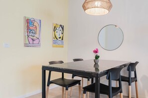 Un espace repas comprenant une table, des chaises, un vase avec des fleurs, un luminaire suspendu et deux œuvres d’art accrochées au mur.