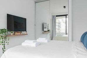 Una habitación de hotel moderna con una cama, un televisor de pantalla plana, un espejo y un balcón con toallas.
