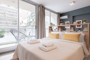 A modern hotel room with a large bed, a balcony with a chair, and a view of the city.