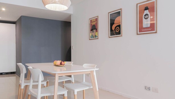 Ein Essbereich mit einem weißen Tisch und Stühlen, einer Obstschale und drei gerahmten Postern an der Wand.
