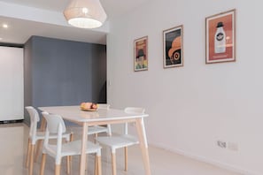 Un coin repas avec une table et des chaises blanches, un panier de fruits et trois affiches encadrées accrochées au mur.