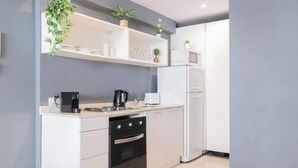 Eine moderne Küche mit weißen Schränken, einem Backofen, einer Mikrowelle und einer Kaffeemaschine. Über der Arbeitsfläche befinden sich Regale mit Gläsern und einem Blumentopf.