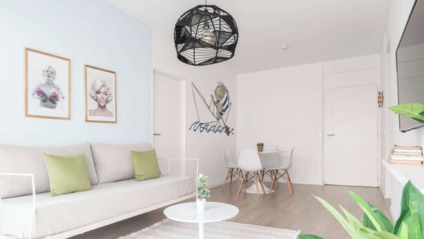 A modern living room with a white sofa, a round coffee table, and a dining area with a white table and chairs.