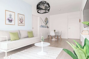 Un salon moderne avec un canapé blanc, une table basse ronde et un coin repas comprenant une table et des chaises blanches.