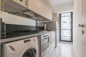 Une cuisine compacte équipée d’un lave-linge, d’un four et d’une fenêtre donnant sur un balcon.