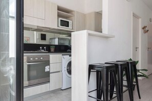 Une cuisine moderne équipée d’un four encastré, d’un four à micro-ondes et d’un lave-linge. On y trouve des tabourets noirs et une plante en pot.