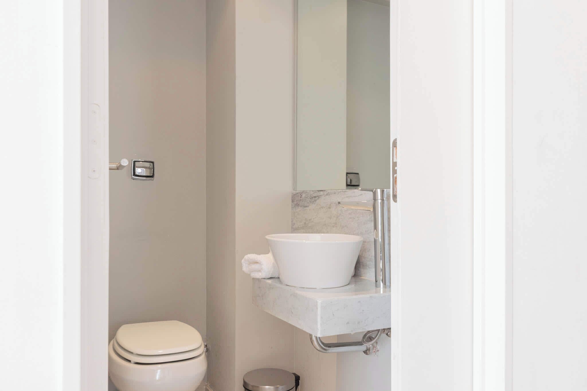 Un baño moderno con inodoro blanco, lavamanos de mármol y un espejo grande.