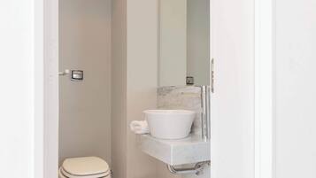 Un baño moderno con inodoro blanco, lavamanos de mármol y un espejo grande.