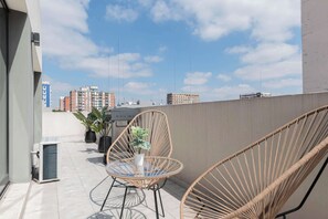 A balcony with wicker chairs, a small round table, and potted plants.