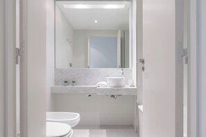 A modern bathroom with a white sink, mirror, and two toilets.