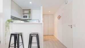 A modern kitchen with white cabinets, a microwave, and two black stools. - MOT Rentals + Zapiola 2300 'D' - Loft Belgrano (Belgrano)