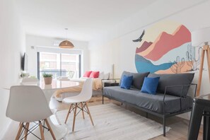Una sala de estar moderna con un sofá gris, sillas blancas, una mesa de comedor y un mural abstracto de gran tamaño en la pared.